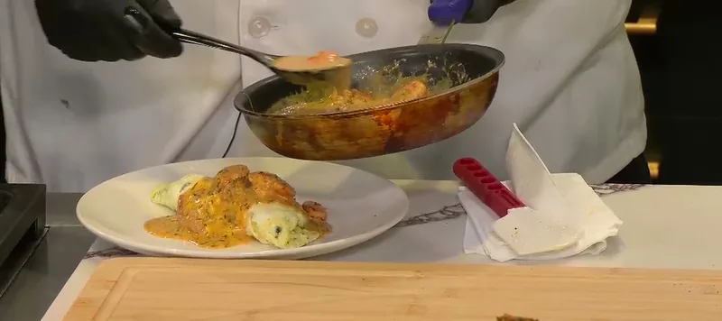 Chef Charles Wilford Sr. spooning shrimp and crawfish sauce from a pan over a plated spinach omelet