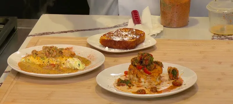 Three plated dishes on the FOX 8 counter: the sauced New Orleans omelet, French toast dusted with powdered sugar, and the barbecue shrimp and crawfish biscuit