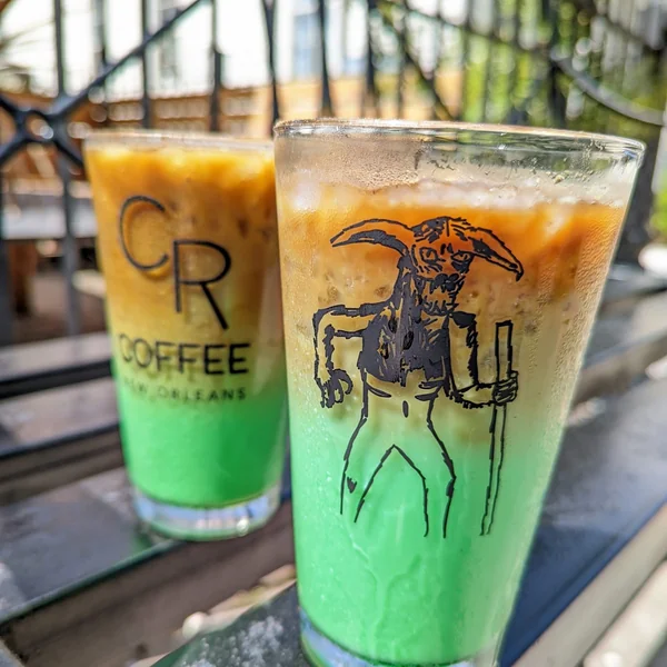 Two iced pandan lattes from CR Coffee, bright green at the bottom under a layer of coffee, one glass printed with the Bayou Beast illustration