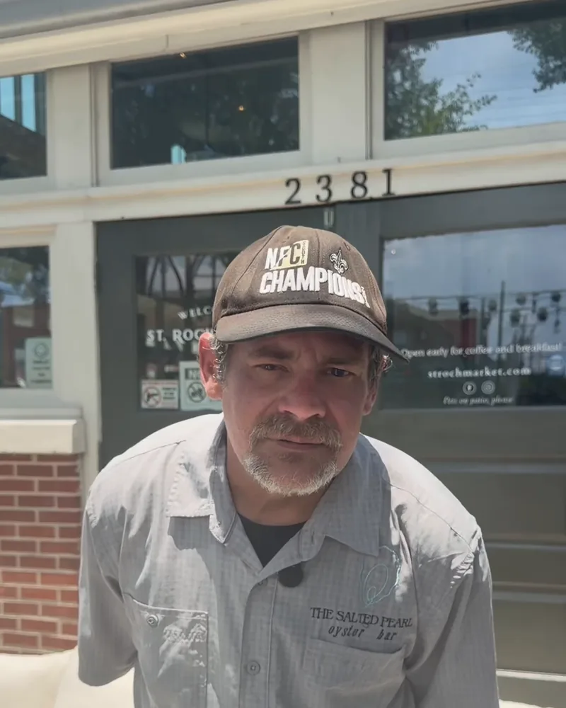 Tyger of Salted Pearl Oyster Bar in a Saints cap standing in front of the St. Roch Market entrance at 2381 St. Claude Ave