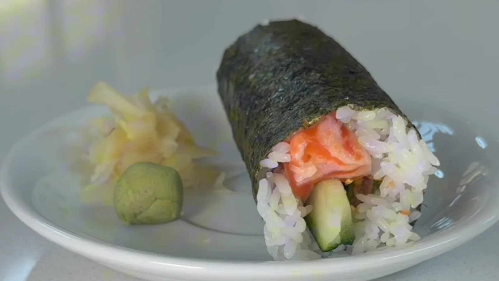 A salmon hand roll at Lin's Poke & Sushi: salmon, cucumber, and avocado wrapped in nori and sushi rice, with pickled ginger and wasabi on the plate