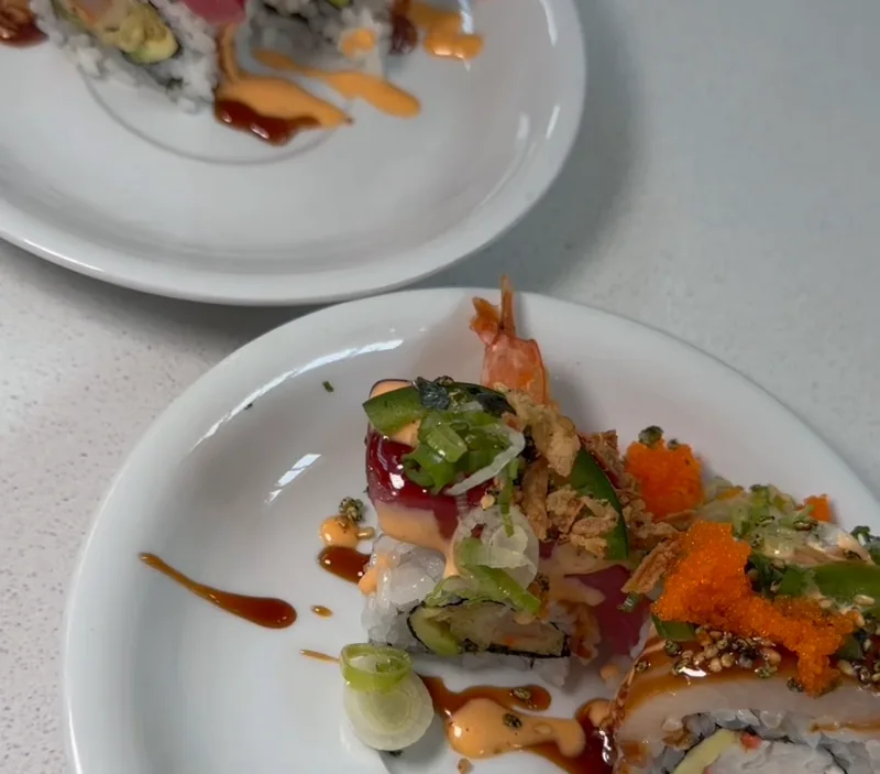 Specialty rolls at Lin's Poke & Sushi topped with tuna, shrimp tempura, fish roe, scallions, and house sauces on white plates