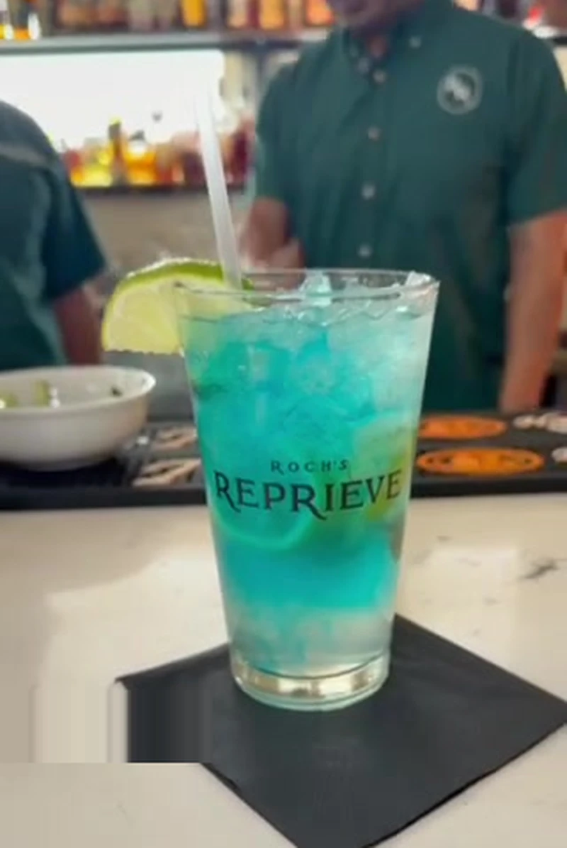 The Shoreline cocktail at Roch's Reprieve, bright blue with a lime wedge garnish in a Roch's Reprieve pint glass