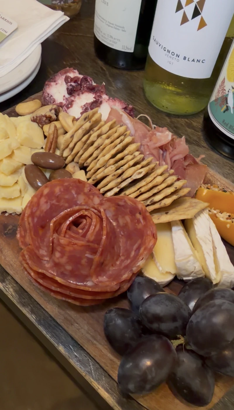 An Olive and Co charcuterie board with salami rose, cheeses, and a bottle of Sauvignon Blanc on the counter at St. Roch Market